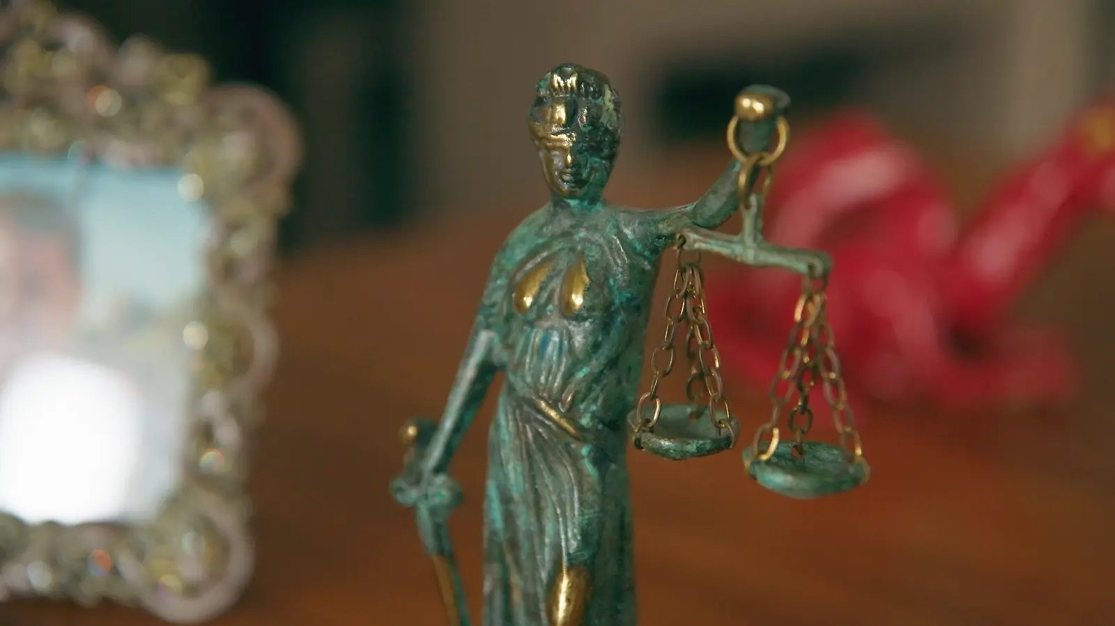 A small bronze Lady Justice statue on a desk beside a framed photo, in warm light.