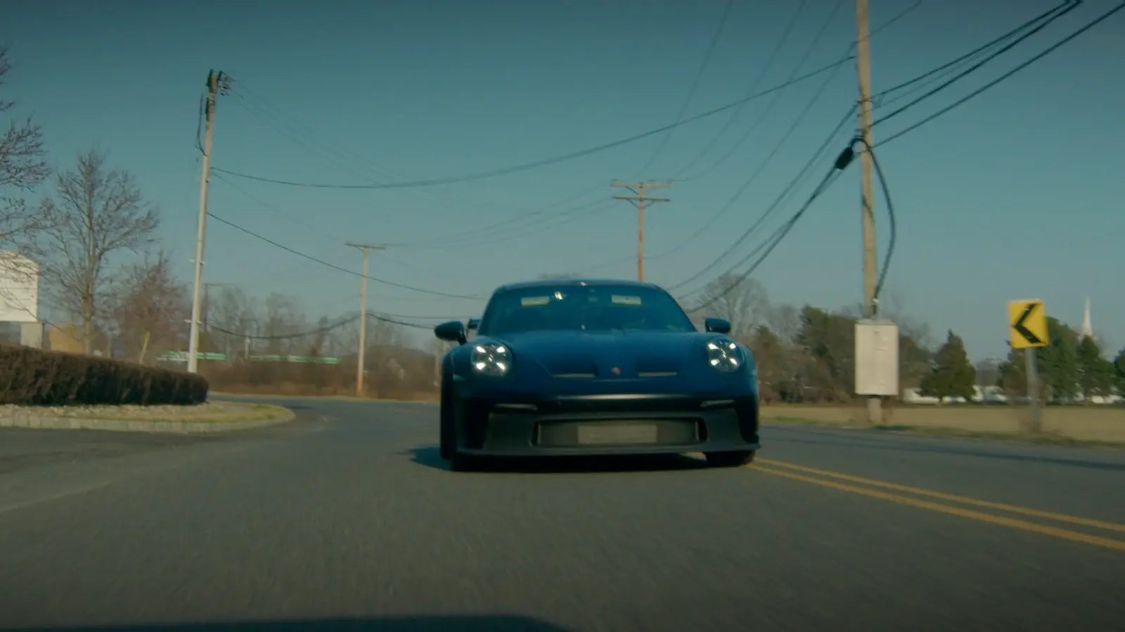 A dark blue sports car on an open country road under a clear sky.