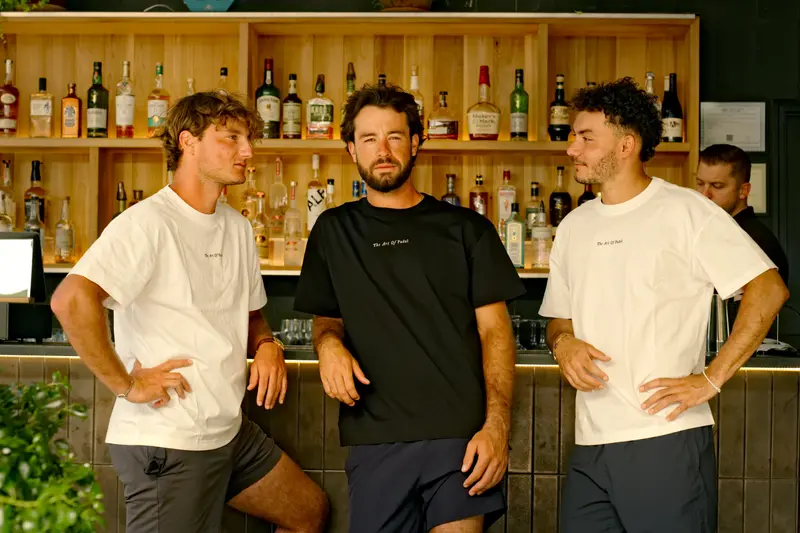 Three men in the campaign’s tees leaning on a clubhouse bar, bottles lit behind them.