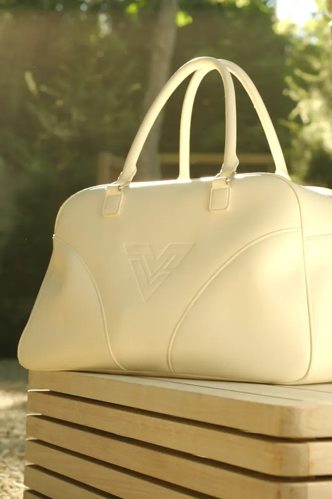 A cream leather duffel on a wooden bench in the late sun.