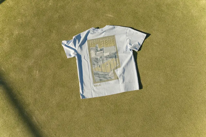A white graphic tee laid flat on green grass.