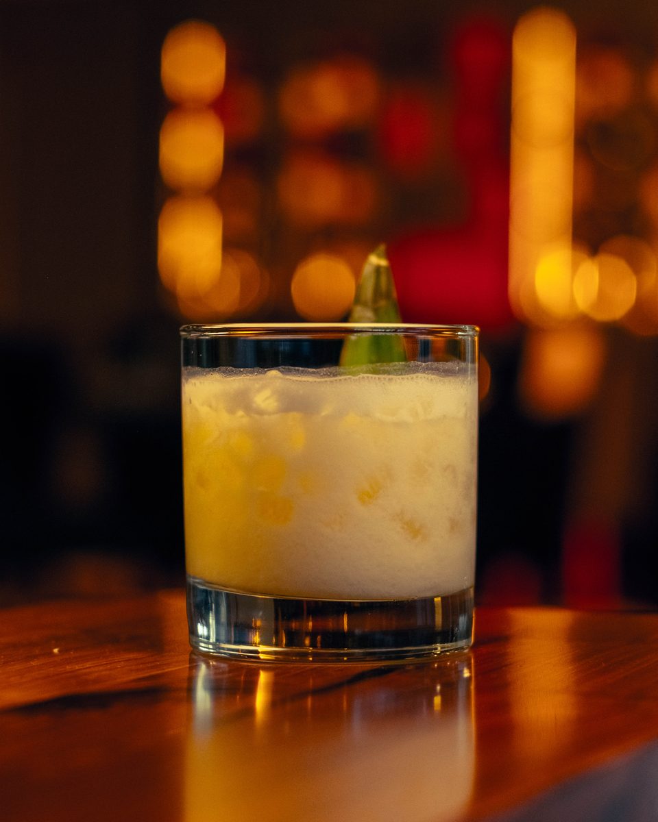 A frothy citrus cocktail on the bar top under the hanging lights.
