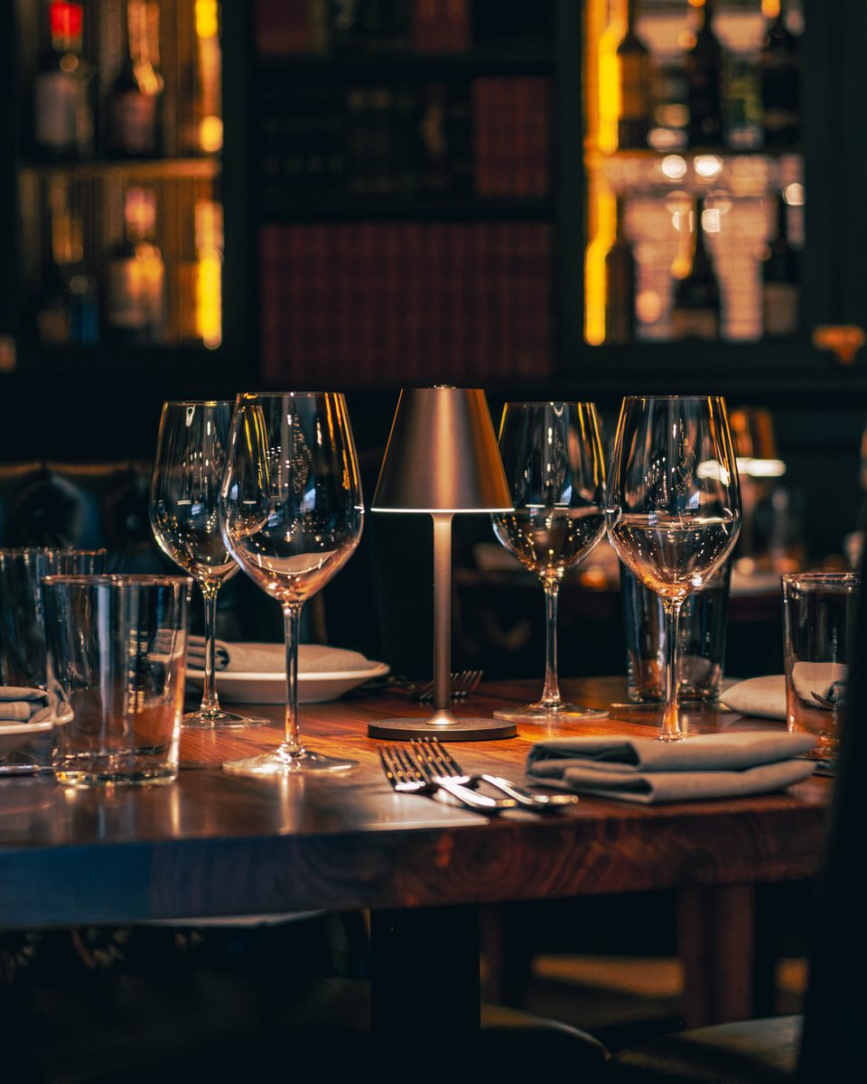 A table set for service, glassware waiting under the bottle wall.